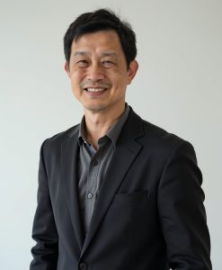 Professional headshot of a smiling middle-aged Asian man wearing a black blazer over a dark grey button-down shirt.
